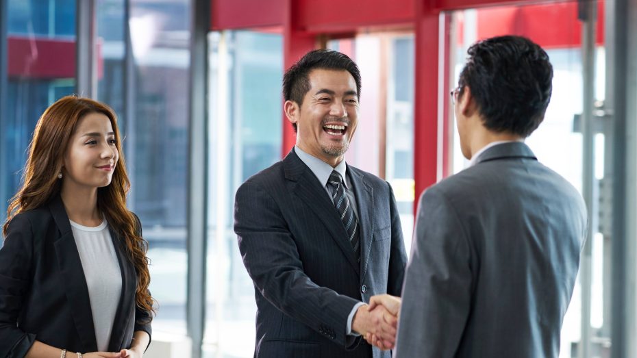 Two men shake hands while a woman stands in the background